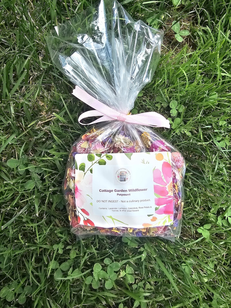 May include: A clear plastic bag filled with dried colorful wildflowers, tied with a light pink ribbon. The white label reads: Cottage Garden Wildflower Potpourri, DO NOT INGEST - Not a culinary product. Contains: Lavender, Larkspur, Calendula, Rose Petals & Yarrow, & other dried flowers.