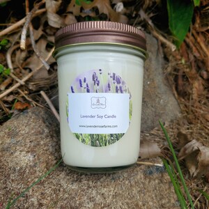 Pode incluir: Uma vela de soja branca em um pote de vidro com tampa de cobre. O r&oacute;tulo apresenta um design de lavanda e o texto "Lavender Soy Candle" e "www.lavenderrosefarms.com".