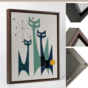 May include: A framed canvas print featuring a mid-century modern design of three stylized cats in shades of blue and green against a white background. The cats are arranged in a playful, abstract composition with a yellow circle in the background.