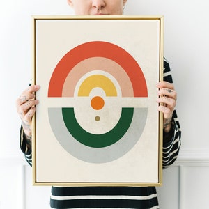 May include: A framed abstract art print featuring a geometric design with a rainbow of colors. The artwork includes a red, pink, yellow, and orange arch, with a green and gray semi-circle below. The frame is gold.