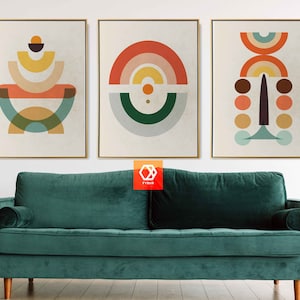 May include: Three framed abstract art prints with geometric shapes in orange, yellow, teal, and brown tones. The artwork hangs above a teal velvet sofa with wooden legs. The room has a minimalist design.