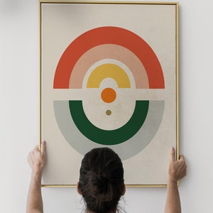 May include: Abstract art print with a gold frame. The artwork features a geometric design with a half-circle in red, pink, and yellow, and a green and gray half-circle below. A small orange circle and a dot are in the center.