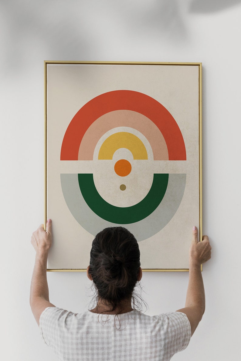 May include: Abstract art print with a gold frame. The artwork features a geometric design with a half-circle in red, pink, and yellow, and a green and gray half-circle below. A small orange circle and a dot are in the center.