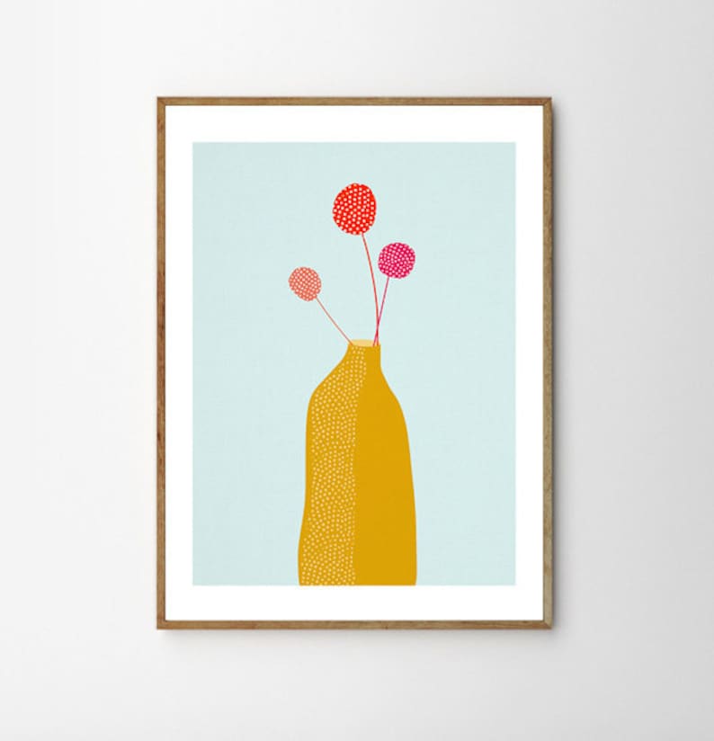 Op de afbeelding: Een ingelijste kunstdruk met een gele vaas met een stippenpatroon, met drie stelen met rode en roze bolvormige bloemen. De achtergrond is lichtblauw en de lijst is van natuurlijk hout.