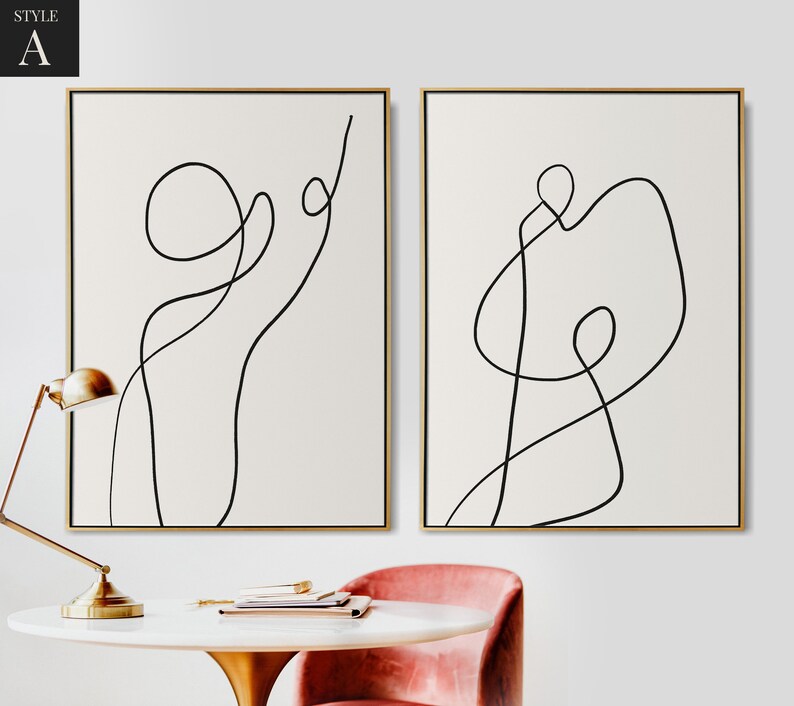 May include: Two minimalist line art prints in black and white on a white background. The prints are framed in gold and feature abstract line drawings.