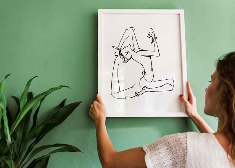 May include: A white framed print of a black and white line drawing of a person in a yoga pose.