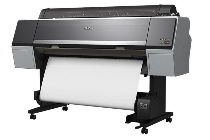 May include: A large format Epson SureColor printer with a roll of white paper feeding through it. The printer is black and silver with a black base and wheels.