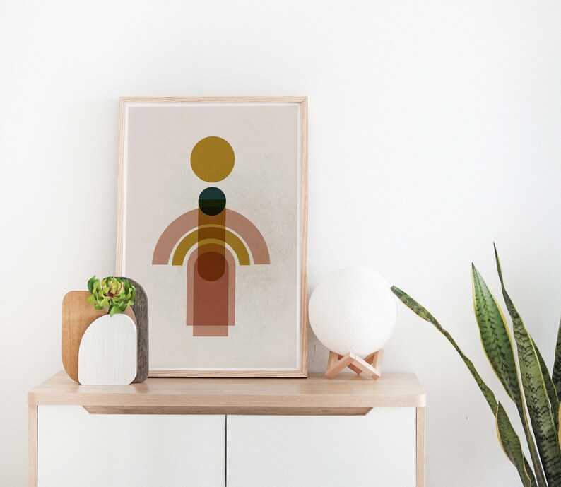 May include: A framed print with a minimalist geometric design featuring a yellow circle, a dark green circle, and overlapping pink and brown arches on a beige background.