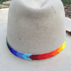 May include: A grey felt cowboy hat with a colourful beaded band. The band is made of small beads in shades of blue, green, red, orange, and yellow.
