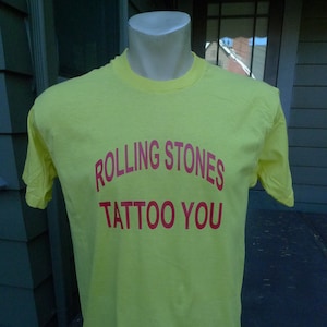 May include: Yellow t-shirt with the text "Rolling Stones Tattoo You" in red.