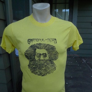 May include: Yellow t-shirt with a black and white graphic of a man with a beard and the text "Grateful Dead" printed on the front.