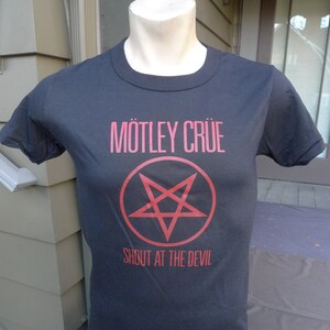 以下が含まれることがあります： 黒いTシャツに赤い「Mötley Crüe」のロゴと円の中に五芒星が描かれている。ロゴの下には「Shout at the Devil」の文字が印刷されている。
