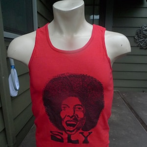May include: Red tank top with a black and white graphic of Sly Stone's face and the word "SLY" printed on the front.