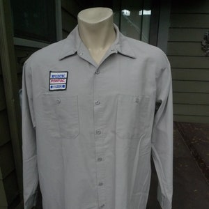 以下が含まれることがあります： 左胸に「Buick Pontiac Service」と書かれたパッチが付いた、薄いグレーの長袖作業シャツです。
