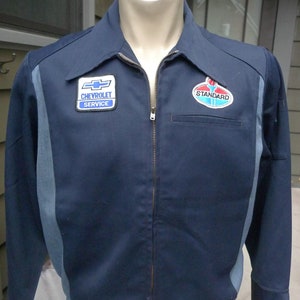 May include: A dark blue work jacket with a zipper closure and two patches. The left patch says "Chevrolet Service" and the right patch says "Standard".