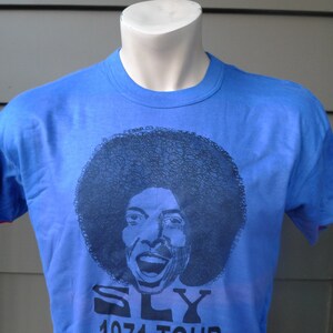 May include: A blue t-shirt with a black and white image of Sly Stone and the text "SLY 1971 TOUR".