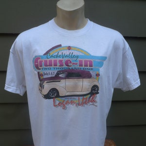 May include: White t-shirt featuring a graphic for the Cache Valley Cruise-In car show. The design includes a classic car illustration, the event name, and the text "TWO THOUSAND ONE" and "July 5,6,7".