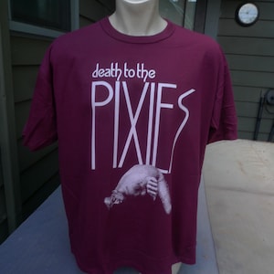 Puede incluir: Camiseta granate con la frase "death to the PIXIES" en blanco. Debajo, una ilustración en escala de grises de una criatura. La camiseta se exhibe en un maniquí.