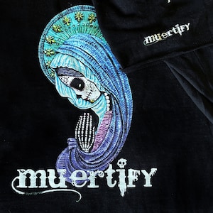 Puede incluir: Camiseta negra con una ilustraci&oacute;n azul y morada de una mujer con cara de calavera y la palabra "muertify" impresa en blanco.