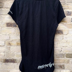 Puede incluir: Camiseta negra con un gr&aacute;fico blanco que dice "muertify" en el dobladillo inferior.