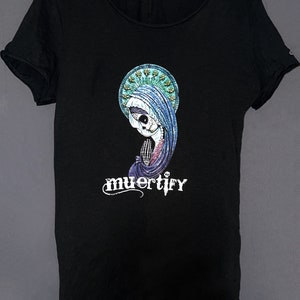 Puede incluir: Camiseta negra con un estampado gr&aacute;fico de un esqueleto con una t&uacute;nica azul y un halo. El texto "muertify" est&aacute; impreso debajo del gr&aacute;fico.