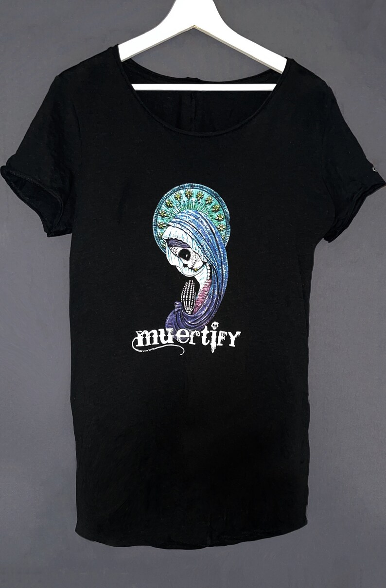Puede incluir: Camiseta negra con un estampado gr&aacute;fico de un esqueleto con una t&uacute;nica azul y un halo. El texto "muertify" est&aacute; impreso debajo del gr&aacute;fico.