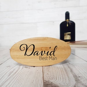 May include: A light brown oval-shaped wooden brush with the text "David Best Man" engraved on it.