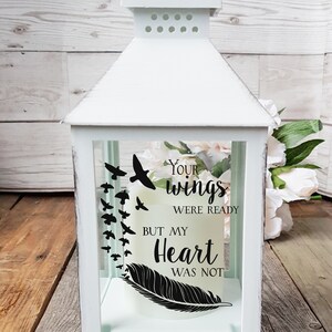 May include: White lantern with a glass panel featuring a black feather and the text "Your wings were ready but my heart was not".  The glass panel also features a silhouette of birds flying away.
