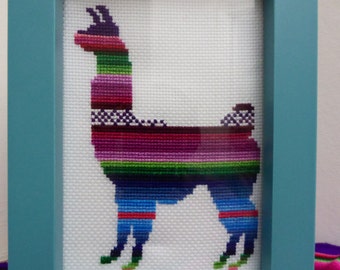 May include: A framed cross-stitch of a colorful llama with a blue frame. The llama is depicted in a side profile with a striped pattern of purple, pink, green, and blue.