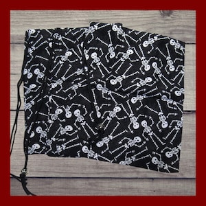 May include: Black drawstring bag with a repeating pattern of white skeletons. The bag is made of a soft fabric and has a black drawstring closure. The bag is designed for carrying items and has a spooky, Halloween theme.