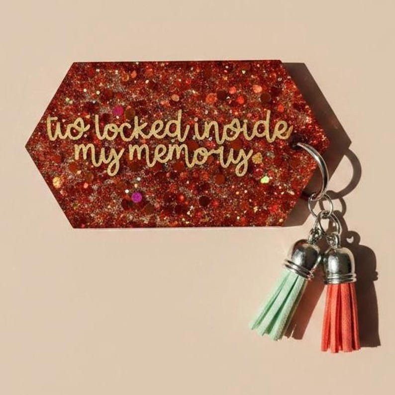 May include: A red glitter keychain with the text "to locked inside my memory". The keychain has a silver ring and two tassels, one mint green and one coral.