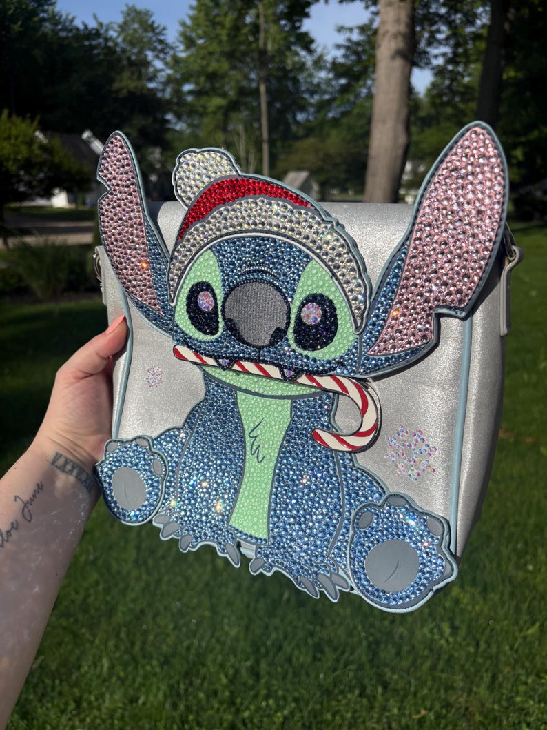 Pu&ograve; includere: Borsa a tracolla argentata con un design Stitch scintillante. Il personaggio blu &egrave; adornato con strass e un cappello da Babbo Natale, che tiene in mano un bastoncino di zucchero. La borsa ha una tracolla argentata ed &egrave; decorata con fiocchi di neve.