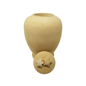May include: A beige ceramic urn with a lid featuring two star-shaped details. The urn has a rounded body and a slightly flared opening.