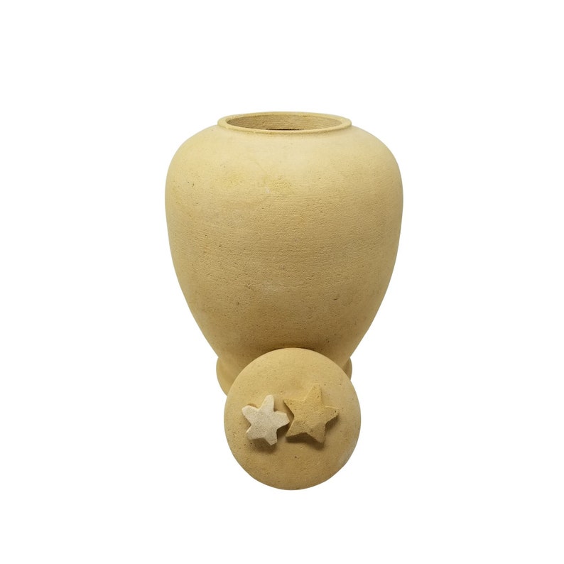 May include: A beige ceramic urn with a lid featuring two star-shaped details. The urn has a rounded body and a slightly flared opening.