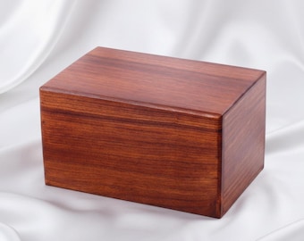 Peut inclure: Une boîte rectangulaire en bois avec une finition lisse et polie d'une riche couleur brun rougeâtre. La boîte présente un motif de grain de bois naturel visible s'étendant horizontalement sur les surfaces avant et supérieure, aux bords nets.
