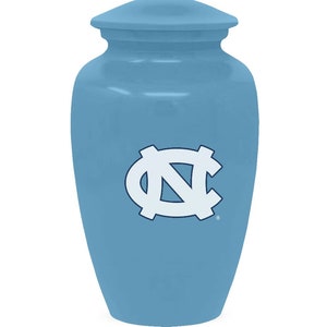 Puede incluir: Una urna de cer&aacute;mica azul claro con un logotipo blanco y azul de los North Carolina Tar Heels.