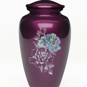 May include: A purple metal urn with a floral design featuring two white roses and leaves. The roses have a pearlescent iridescent finish.