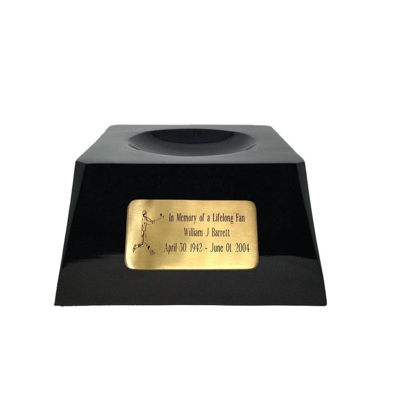 May include: A black, glossy baseball display stand with a recessed top. A gold-colored plaque on the front reads "In Memory of a Lifelong Fan William J Barrett April 30, 1942 - June 01, 2004" with a baseball player illustration.