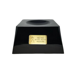 May include: A black, glossy trophy base with a recessed top. A gold-colored plaque features a football player illustration and the inscription: "William J. Barrett April 30, 1943 - June 01, 2004 Always in my Heart."