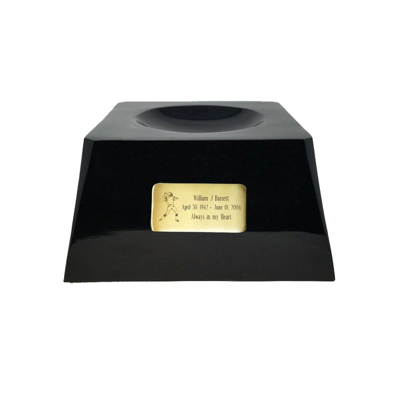 May include: A black, glossy trophy base with a recessed top. A gold-colored plaque features a football player illustration and the inscription: "William J. Barrett April 30, 1943 - June 01, 2004 Always in my Heart."