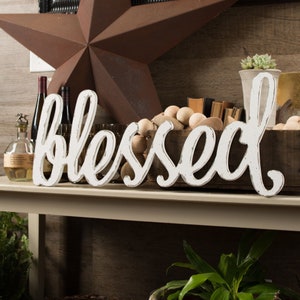 May include: White wooden sign with the word "blessed" in a cursive font. The sign is distressed and has a rustic look.