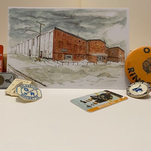 May include: A collection of hockey memorabilia including a vintage hockey card, a small metal keychain with a hockey puck charm, a white and blue plastic pin with the words "Goderich Ringette", a small orange and black button with the words "Oro Ringette", and a gold pin with a blue and white hockey stick design.