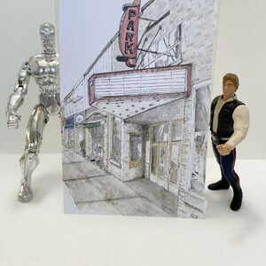 May include: A black and white drawing of a vintage movie theater with a red marquee sign that says "PARK" in a curved font. The building has a brick facade and is located on a street with other buildings in the background.