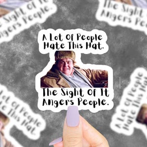 Op de afbeelding: Een sticker met een man die een bruine wintermuts en een jas draagt. De tekst op de sticker luidt "A Lot Of People Hate This Hat. The Sight Of It Angers People."