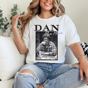 Puede incluir: Camiseta blanca con una foto en blanco y negro de un hombre con el texto "DAN The Man" impreso en ella.