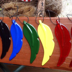 Puede incluir: Siete adornos de plumas de vidrio en diferentes colores, incluyendo negro, azul, verde, amarillo y rojo. Las plumas est&aacute;n suspendidas de cuerdas negras.