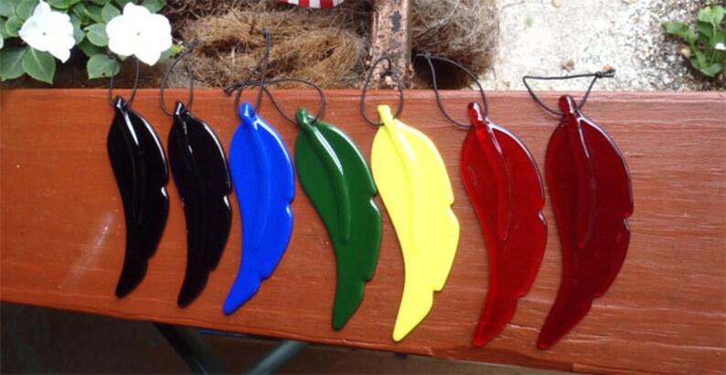 Puede incluir: Siete adornos de plumas de vidrio en diferentes colores, incluyendo negro, azul, verde, amarillo y rojo. Las plumas est&aacute;n suspendidas de cuerdas negras.