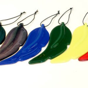Puede incluir: Siete adornos de plumas de vidrio en varios colores, incluyendo negro, morado, azul, verde, amarillo, rojo y granate. Cada pluma est&aacute; suspendida de una cuerda negra.