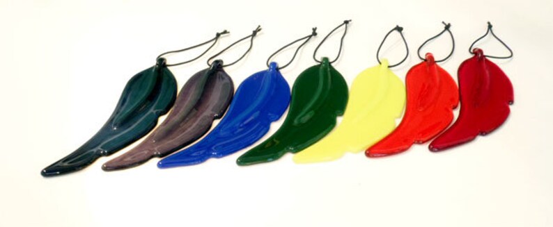 Puede incluir: Siete adornos de plumas de vidrio en varios colores, incluyendo negro, morado, azul, verde, amarillo, rojo y granate. Cada pluma est&aacute; suspendida de una cuerda negra.