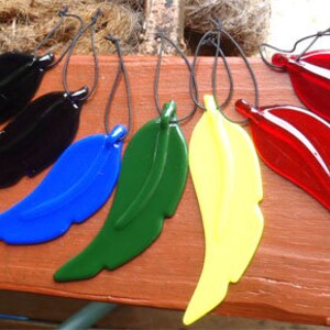 Puede incluir: Seis adornos de plumas de vidrio en varios colores, incluyendo negro, azul, verde, amarillo y rojo. Las plumas cuelgan de cuerdas.